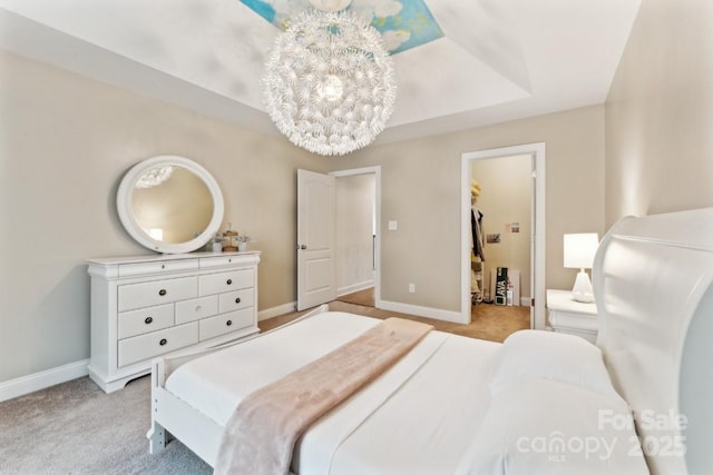 bedroom featuring light carpet, a tray ceiling, a notable chandelier, and baseboards