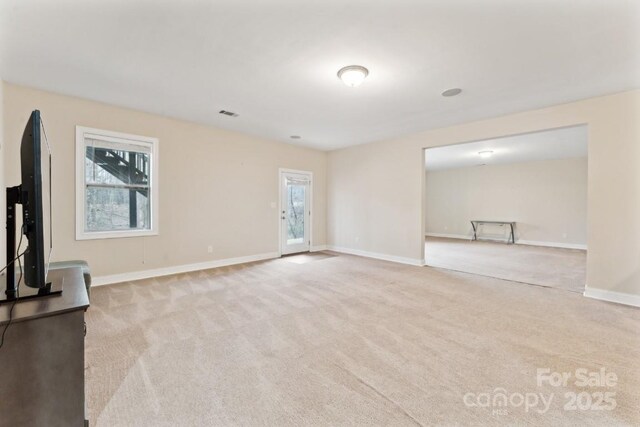 unfurnished living room with light carpet, visible vents, and baseboards