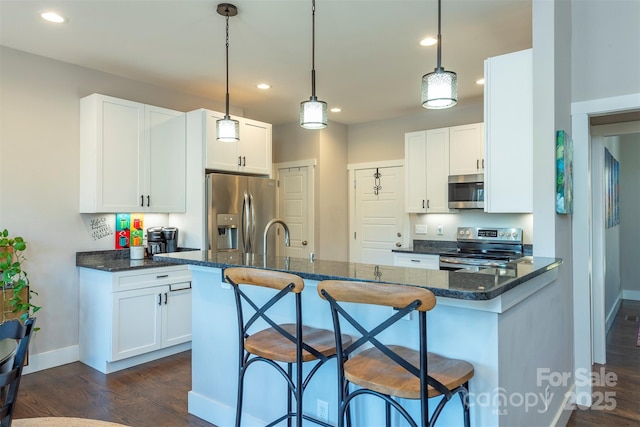 kitchen featuring stainless steel appliances, hanging light fixtures, a breakfast bar area, and white cabinets