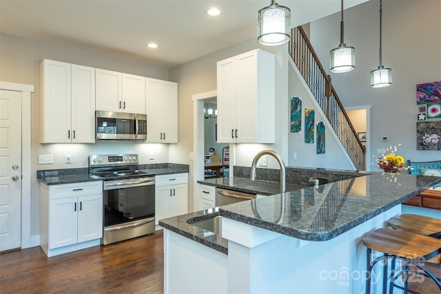 kitchen featuring dark wood-type flooring, hanging light fixtures, dark stone countertops, stainless steel appliances, and white cabinets