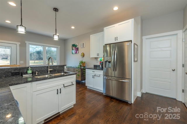 kitchen with pendant lighting, sink, stainless steel fridge, dark stone countertops, and white cabinets