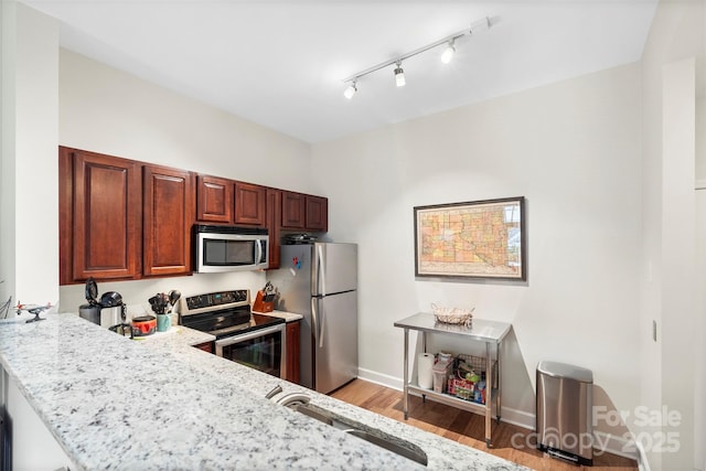 kitchen with kitchen peninsula, light hardwood / wood-style flooring, appliances with stainless steel finishes, sink, and light stone countertops