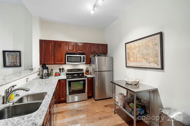 kitchen with light hardwood / wood-style floors, light stone countertops, appliances with stainless steel finishes, rail lighting, and sink