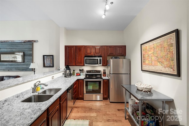 kitchen with appliances with stainless steel finishes, sink, light wood-type flooring, light stone countertops, and rail lighting