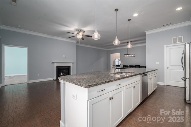 kitchen with appliances with stainless steel finishes, white cabinetry, sink, dark stone countertops, and a center island with sink