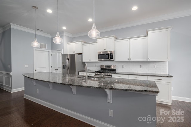 kitchen with decorative light fixtures, white cabinets, appliances with stainless steel finishes, and a kitchen island with sink