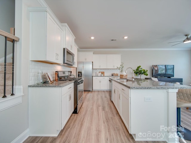 kitchen with sink, white cabinetry, light stone counters, and appliances with stainless steel finishes