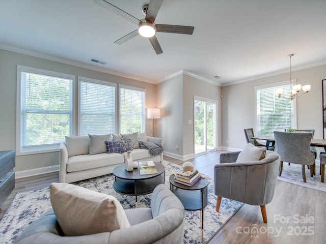 living room featuring ceiling fan with notable chandelier, a healthy amount of sunlight, light hardwood / wood-style flooring, and ornamental molding