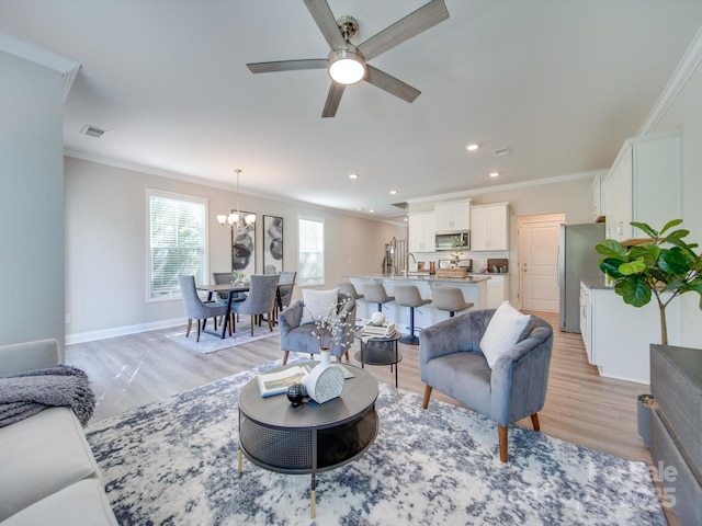 living room featuring light wood-type flooring, ceiling fan with notable chandelier, crown molding, and sink