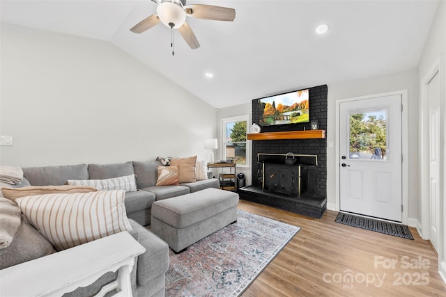 living room featuring ceiling fan, a fireplace, vaulted ceiling, and light hardwood / wood-style flooring