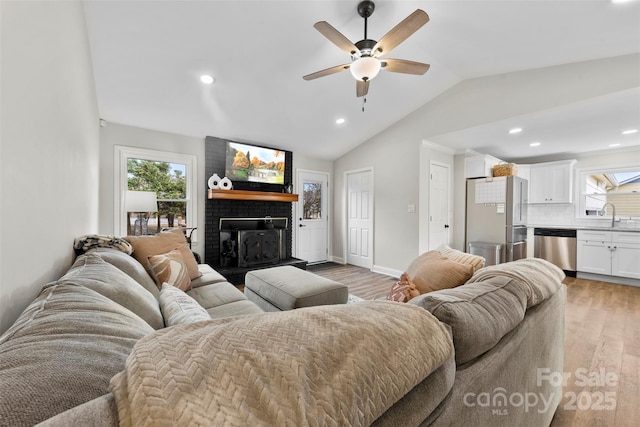 living room with a healthy amount of sunlight, sink, vaulted ceiling, and light hardwood / wood-style flooring