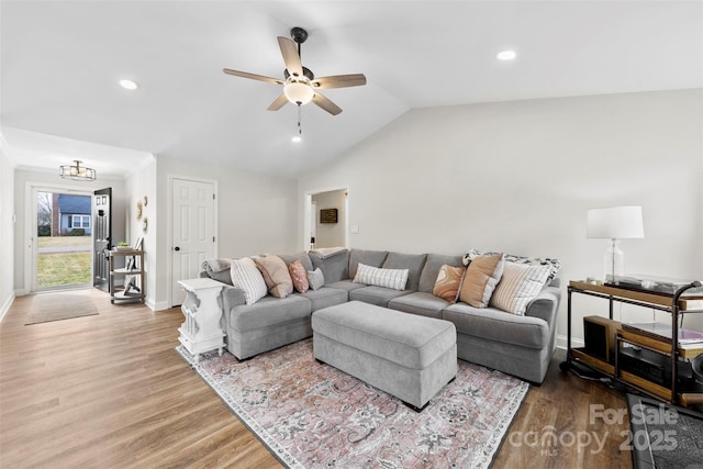 living room with ceiling fan with notable chandelier, vaulted ceiling, and light hardwood / wood-style flooring