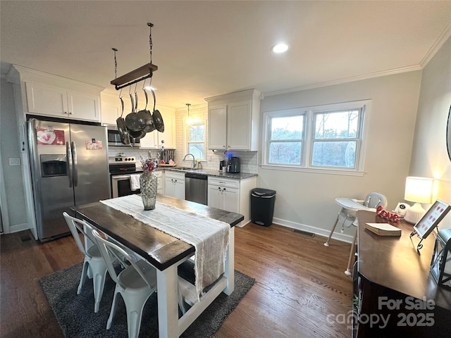 kitchen featuring appliances with stainless steel finishes, white cabinets, hanging light fixtures, crown molding, and dark wood-type flooring