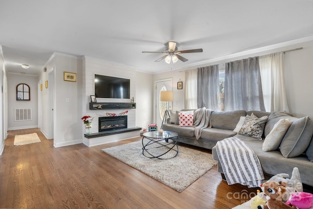 living room featuring a fireplace, crown molding, wood-type flooring, and ceiling fan