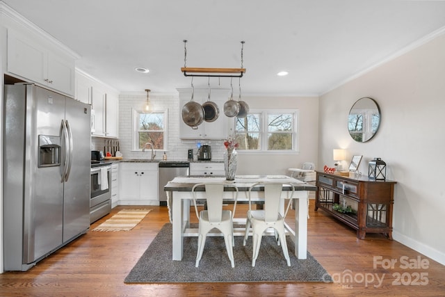 kitchen with appliances with stainless steel finishes, white cabinetry, ornamental molding, a kitchen bar, and decorative light fixtures