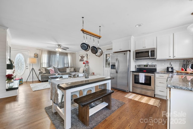 kitchen featuring appliances with stainless steel finishes, dark stone countertops, hardwood / wood-style floors, white cabinetry, and decorative backsplash