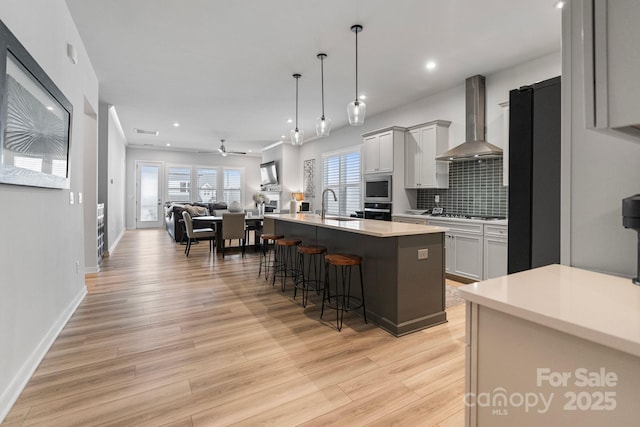 kitchen featuring an island with sink, hanging light fixtures, backsplash, wall chimney range hood, and a kitchen breakfast bar