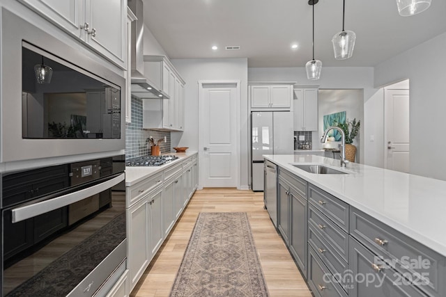 kitchen with white cabinetry, hanging light fixtures, light hardwood / wood-style floors, sink, and wall chimney exhaust hood