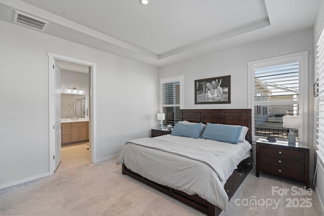 bedroom featuring a tray ceiling, light carpet, ensuite bathroom, and sink