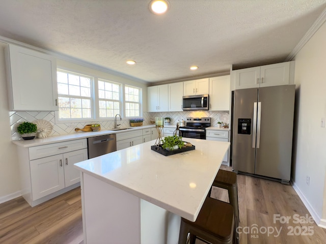 kitchen featuring appliances with stainless steel finishes, white cabinetry, a breakfast bar area, a center island, and crown molding