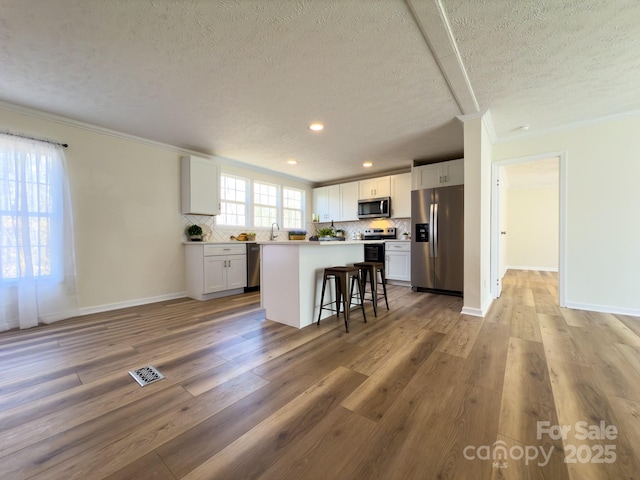 kitchen featuring stainless steel appliances, a center island, white cabinets, and a kitchen bar