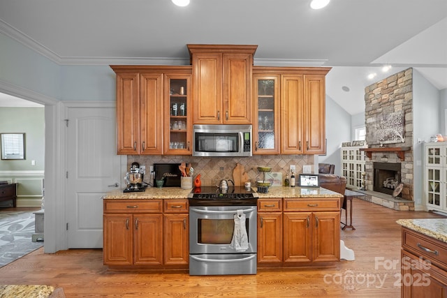 kitchen featuring light wood-type flooring, light stone counters, a fireplace, decorative backsplash, and stainless steel appliances