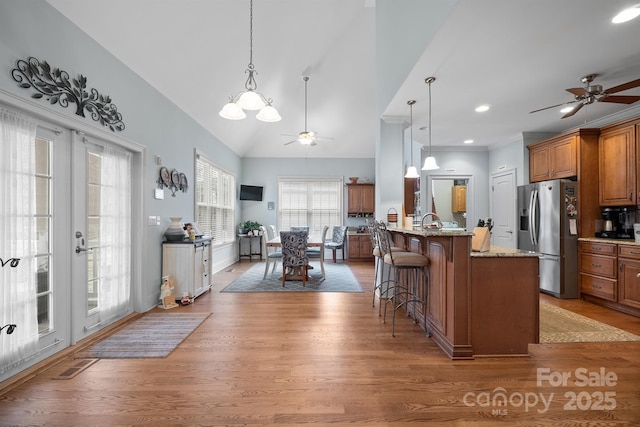 kitchen with a kitchen breakfast bar, stainless steel fridge, hardwood / wood-style flooring, a kitchen island with sink, and lofted ceiling