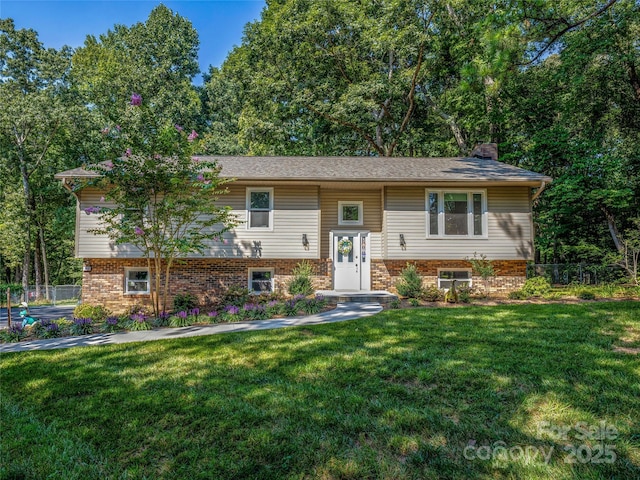 split foyer home with brick siding, a chimney, a front yard, and fence