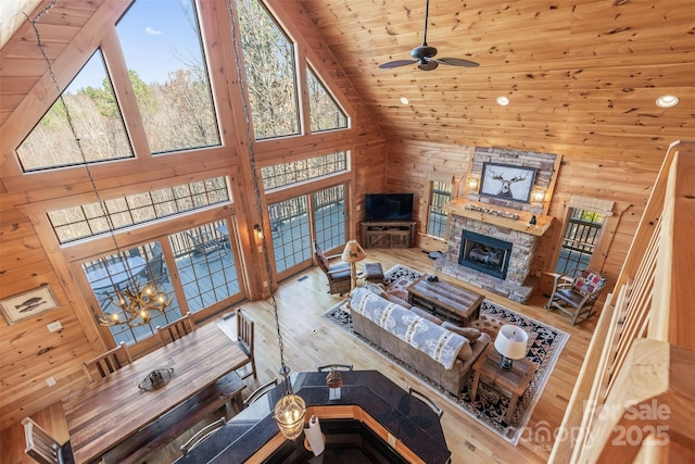 living room with a stone fireplace, wooden walls, high vaulted ceiling, wood ceiling, and light hardwood / wood-style flooring