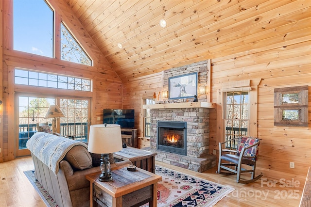 living room featuring a healthy amount of sunlight, a stone fireplace, light hardwood / wood-style flooring, and wood walls