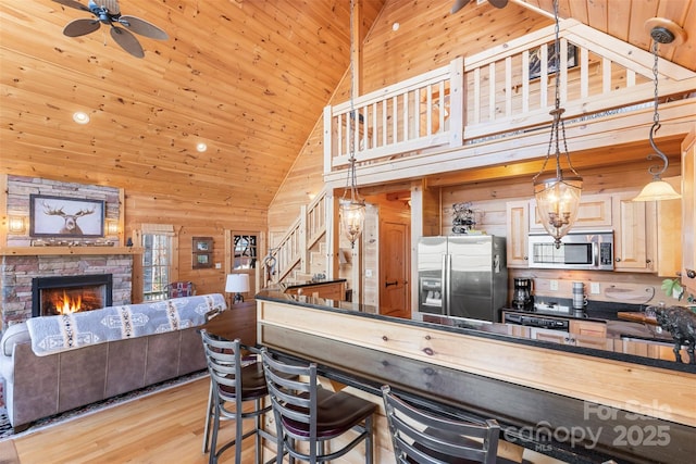 kitchen with stainless steel appliances, ceiling fan, pendant lighting, wood walls, and a fireplace