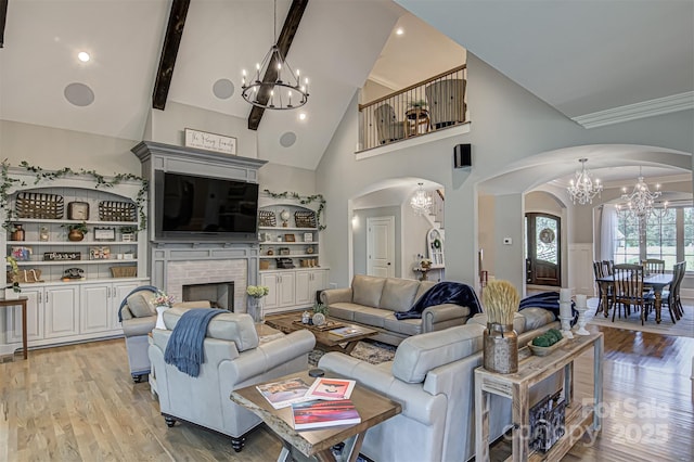 living room featuring high vaulted ceiling, beamed ceiling, a brick fireplace, an inviting chandelier, and light hardwood / wood-style flooring