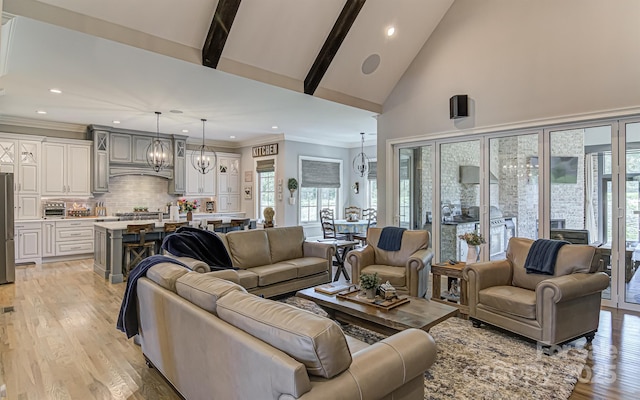 living room featuring a chandelier, high vaulted ceiling, a healthy amount of sunlight, beam ceiling, and light hardwood / wood-style floors