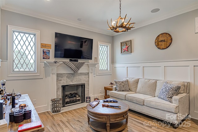 living room with a tile fireplace, crown molding, an inviting chandelier, and light hardwood / wood-style floors