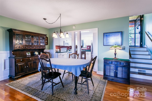 dining room featuring a chandelier, visible vents, baseboards, stairs, and dark wood-style floors