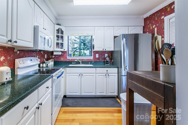 kitchen featuring white appliances, a sink, white cabinetry, dark countertops, and wallpapered walls