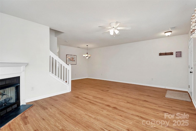 unfurnished living room with ceiling fan with notable chandelier and light wood-type flooring