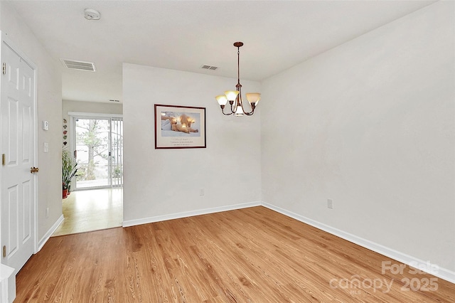 empty room featuring wood-type flooring and a notable chandelier