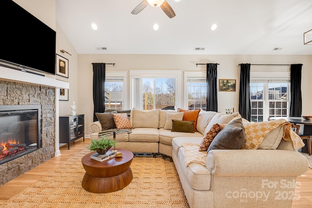 living room featuring ceiling fan, lofted ceiling, a stone fireplace, and light wood-type flooring