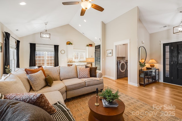 living room featuring ceiling fan with notable chandelier, high vaulted ceiling, light hardwood / wood-style floors, and washer and dryer