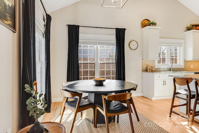 dining space with light hardwood / wood-style flooring, sink, and vaulted ceiling