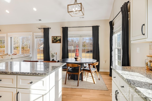 kitchen with white cabinetry, an inviting chandelier, light stone counters, and light wood-type flooring