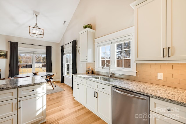 kitchen with lofted ceiling, sink, stainless steel dishwasher, pendant lighting, and white cabinets