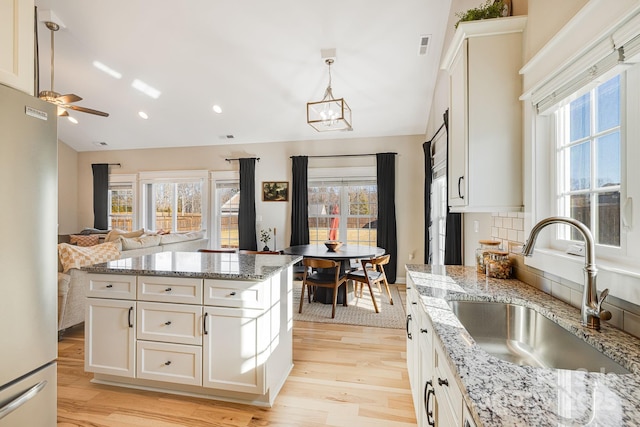 kitchen featuring stainless steel refrigerator, decorative light fixtures, sink, and white cabinets