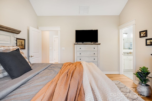 bedroom featuring ensuite bathroom, lofted ceiling, and light wood-type flooring