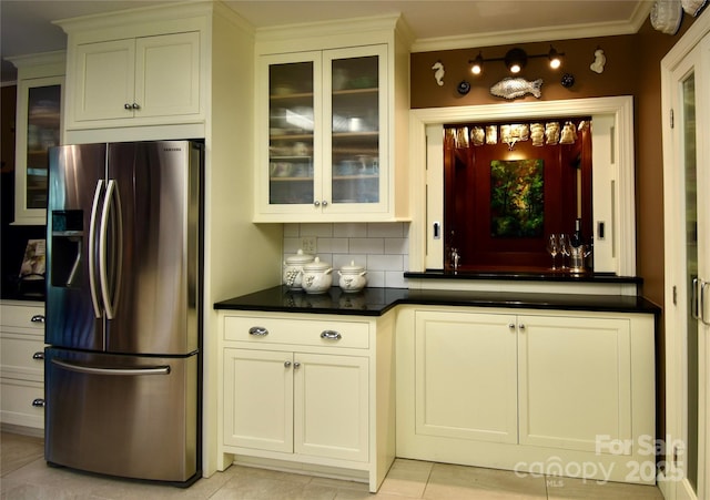 kitchen featuring tasteful backsplash, dark countertops, glass insert cabinets, ornamental molding, and stainless steel fridge