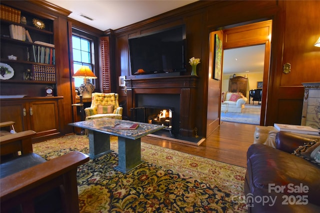 sitting room featuring a lit fireplace, visible vents, and wood finished floors