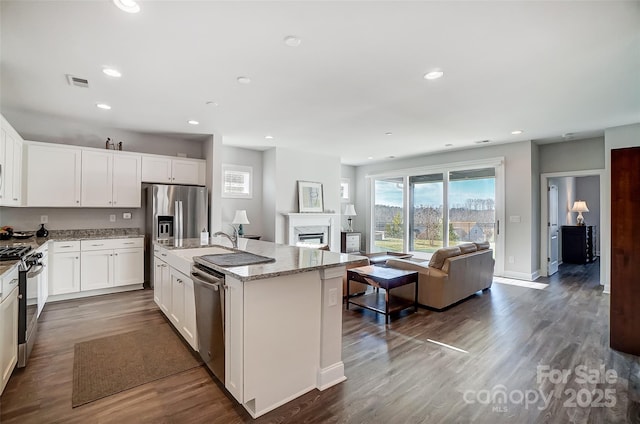 kitchen featuring white cabinets, dark hardwood / wood-style flooring, a kitchen island with sink, stainless steel appliances, and light stone countertops