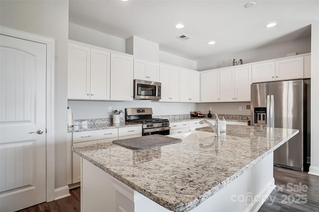 kitchen with light stone countertops, stainless steel appliances, an island with sink, and white cabinets