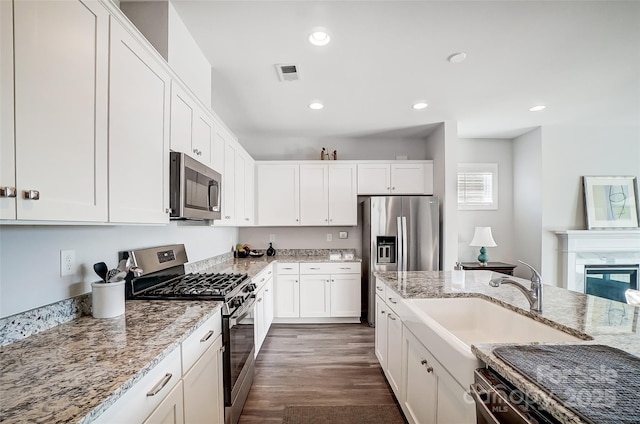 kitchen with white cabinetry, appliances with stainless steel finishes, light stone countertops, and dark wood-type flooring